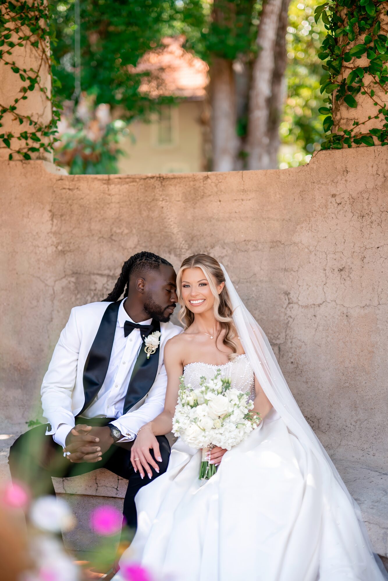 Bride and groom sit close together for portraits by a Tuscan wall