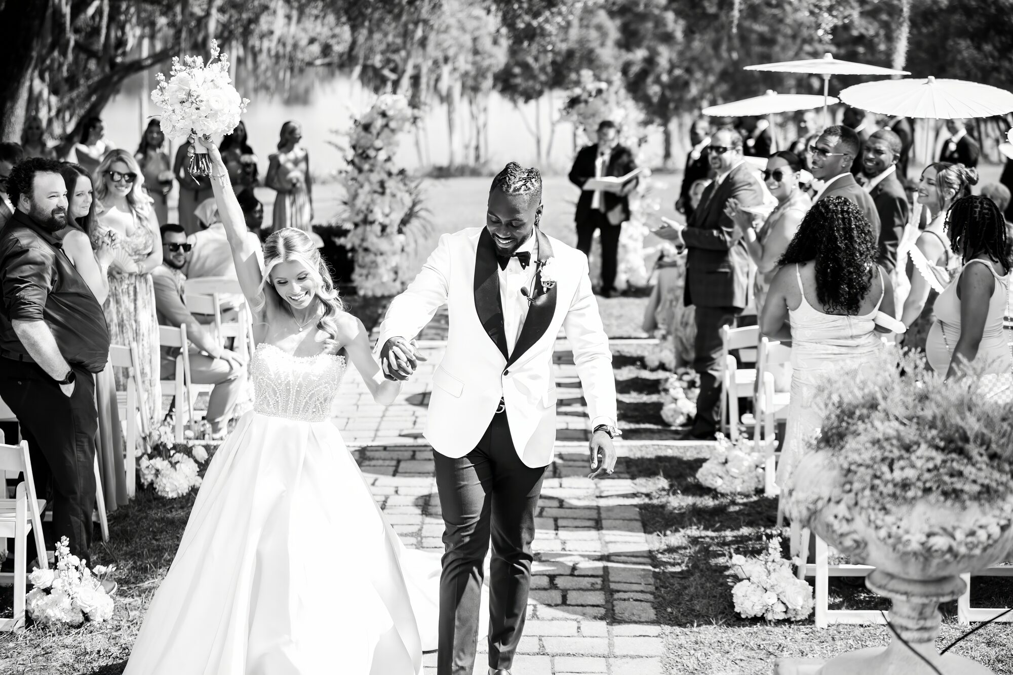 Wide black-and-white view of the outdoor ceremony under the trees